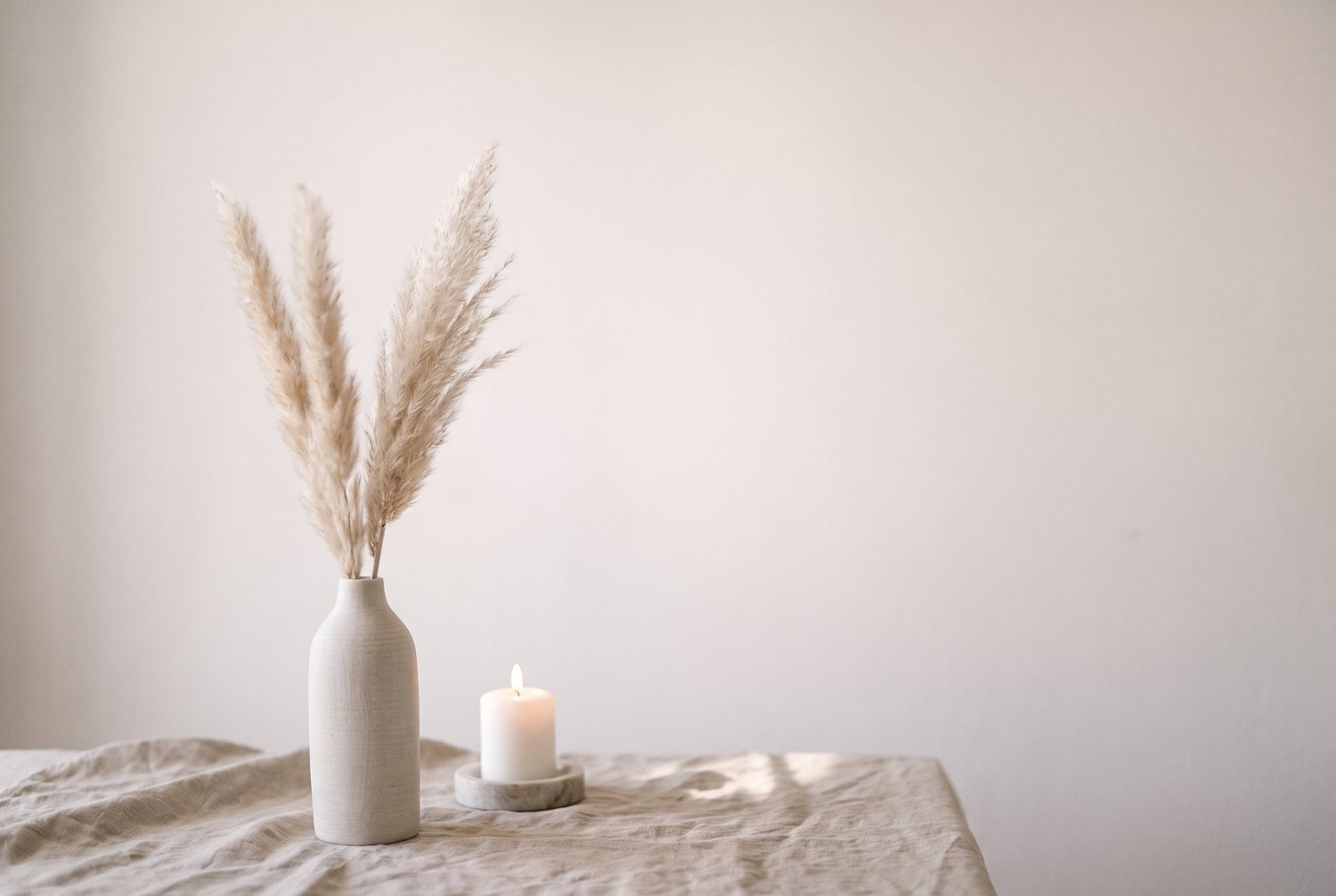 Soft pampas grass and a lit candle on beige linen